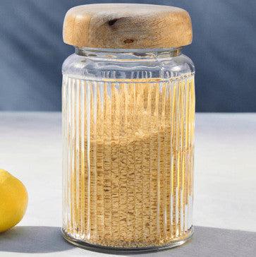 Glass jar with wooden lid containing toothpicks on a white surface.