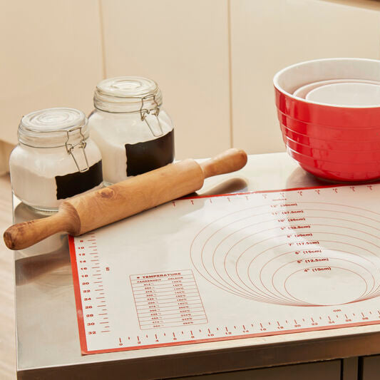 Kitchen counter with red mixing bowl, rolling pin, and measuring cups on a silicone mat.