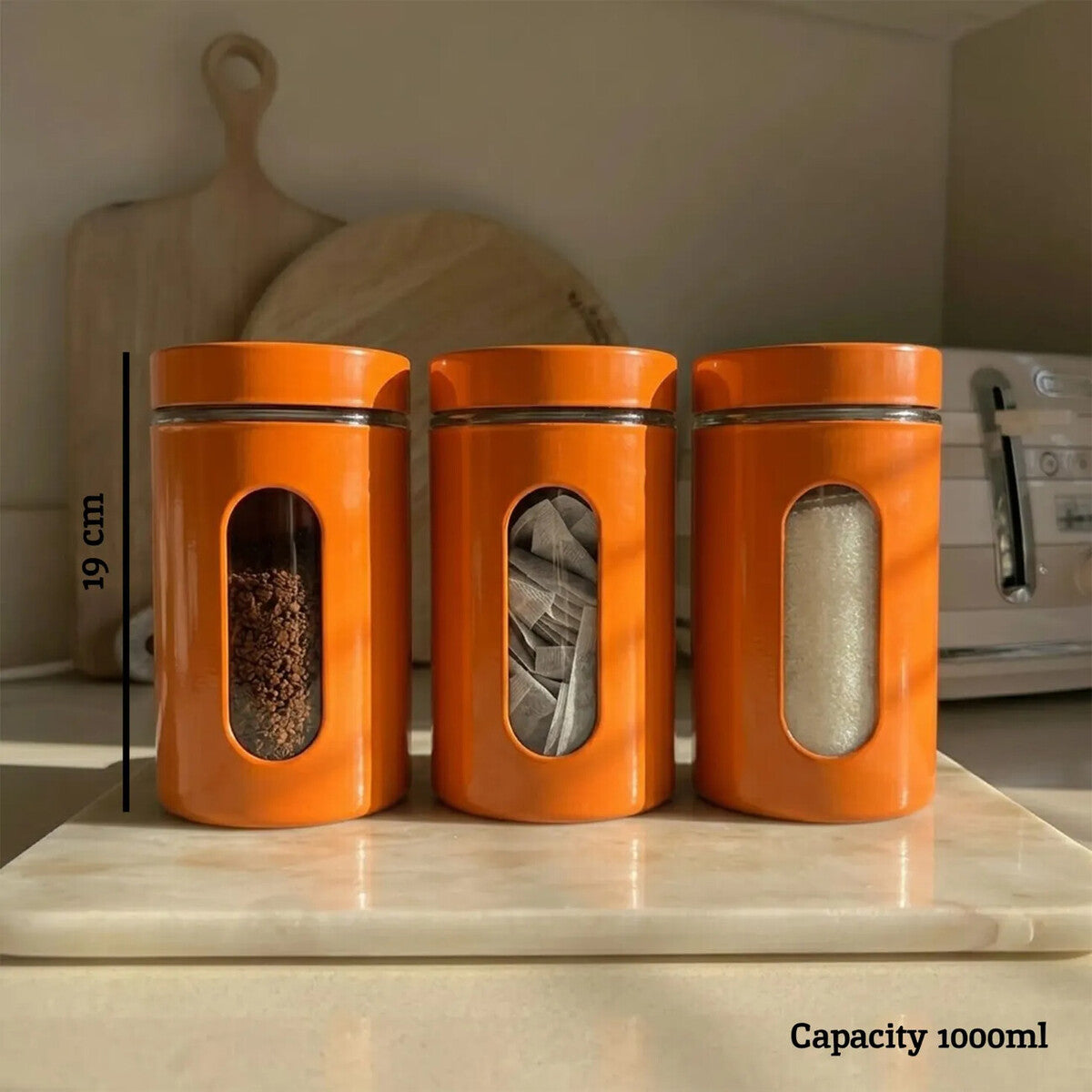 Three orange canisters with windowed lids on a kitchen counter, showing capacity measurement.