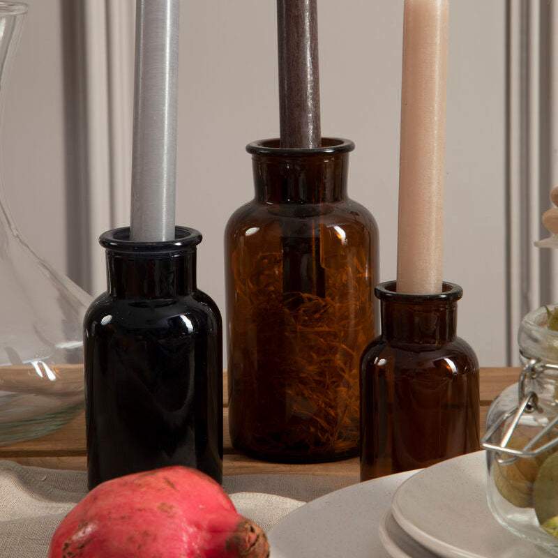Decorative setup with candles in brown bottles on a table.