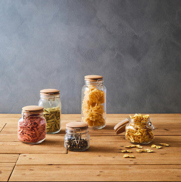 Jars of dried pasta on a wooden table with a gray background