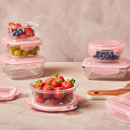 Set of glass food containers with pink lids on a wooden surface with fruits.