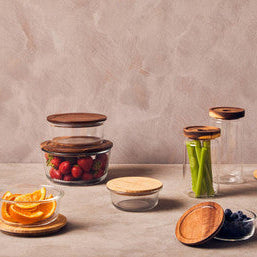 Set of glass containers with wooden lids on a wooden surface with a neutral background