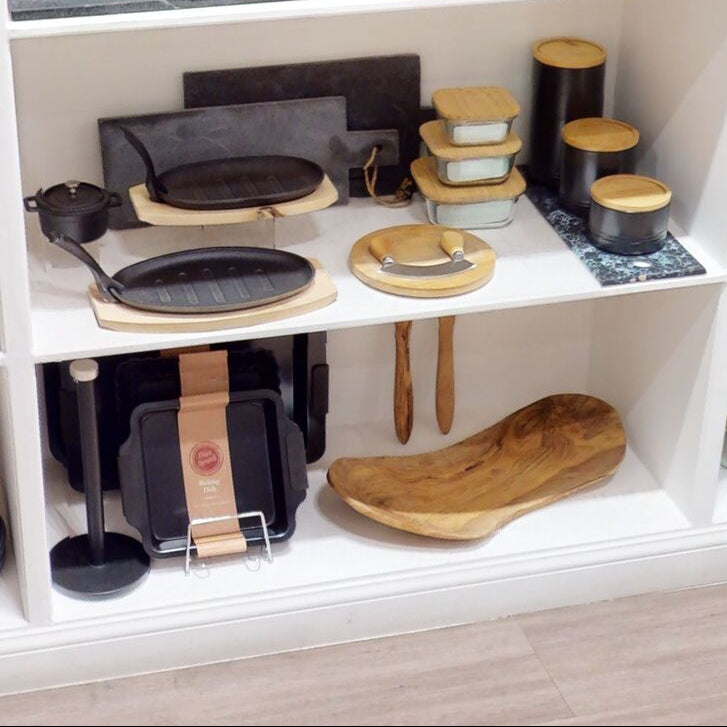 Collection of kitchen utensils including pans, cutting boards, and a wooden ladle on a white shelf.