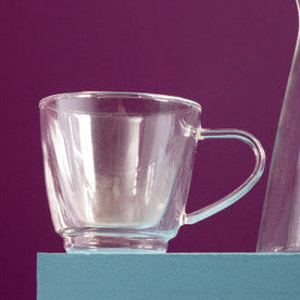 Clear glass mug and metallic pitcher on a teal surface with a purple background