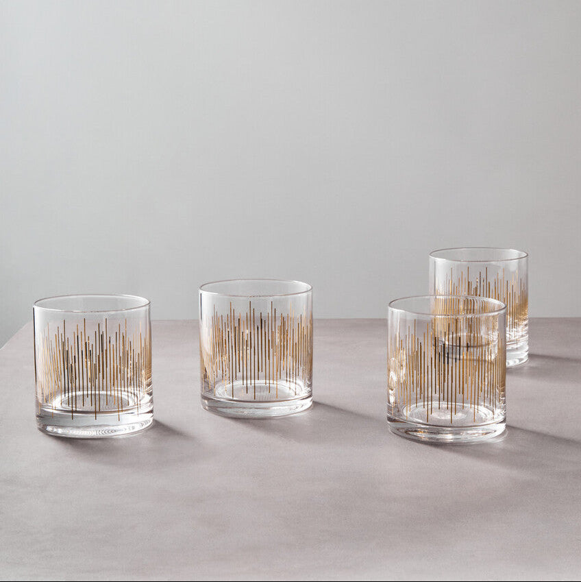 Set of four clear glass tumblers with gold interior patterns on a light gray surface.