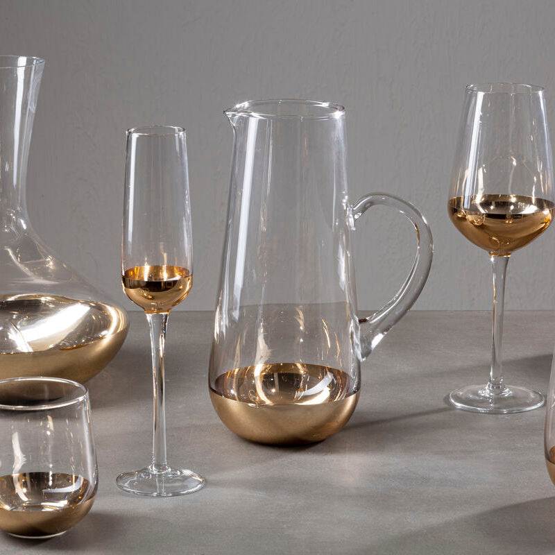 Set of glass wine glasses and decanters with gold accents on a gray surface.