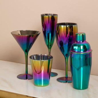 Set of colorful metallic cocktail glasses on a reflective surface with a beige background