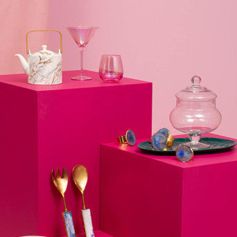 Table setting with pink plates, cutlery, and glasses on a pink background