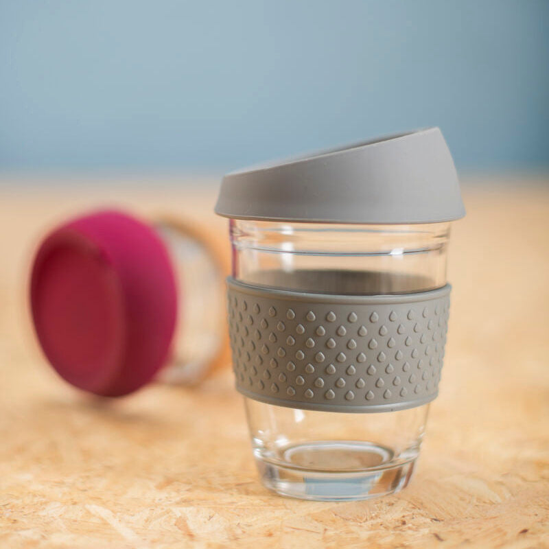 Clear glass cup with gray textured sleeve and lid on a wooden surface