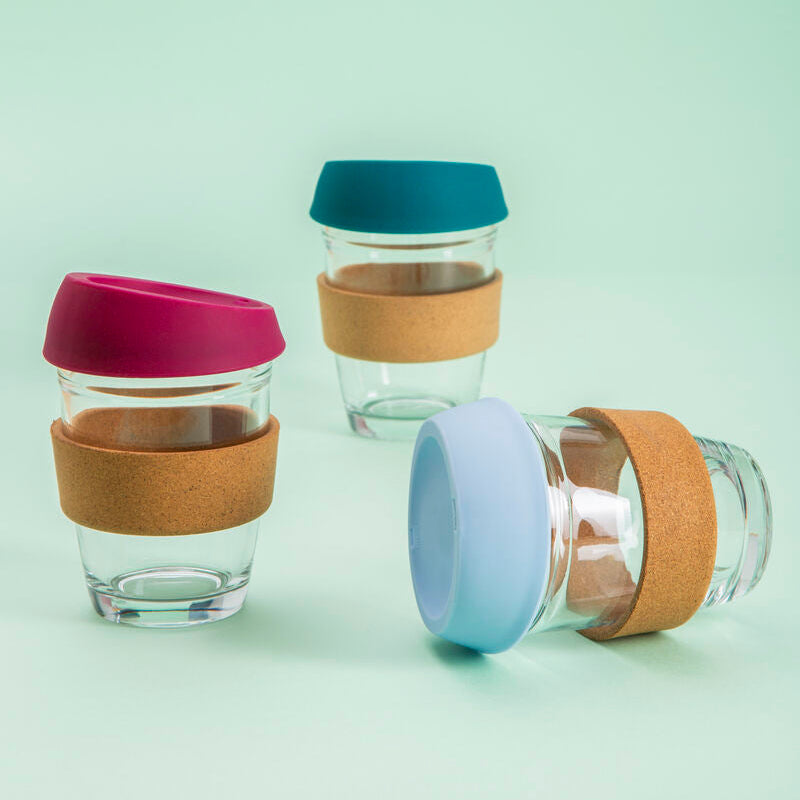Three glass cups with colorful lids and cork bases on a light green background