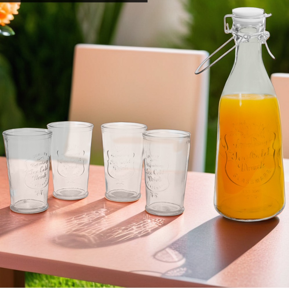 Glass bottle with airtight swing top and glasses on a table outdoors.