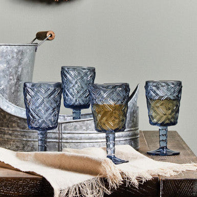 Set of blue glass goblets on a wooden surface with a decorative wreath in the background.