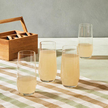 Clear glasses with a light yellow liquid on a striped tablecloth, with a wooden picnic basket in the background.