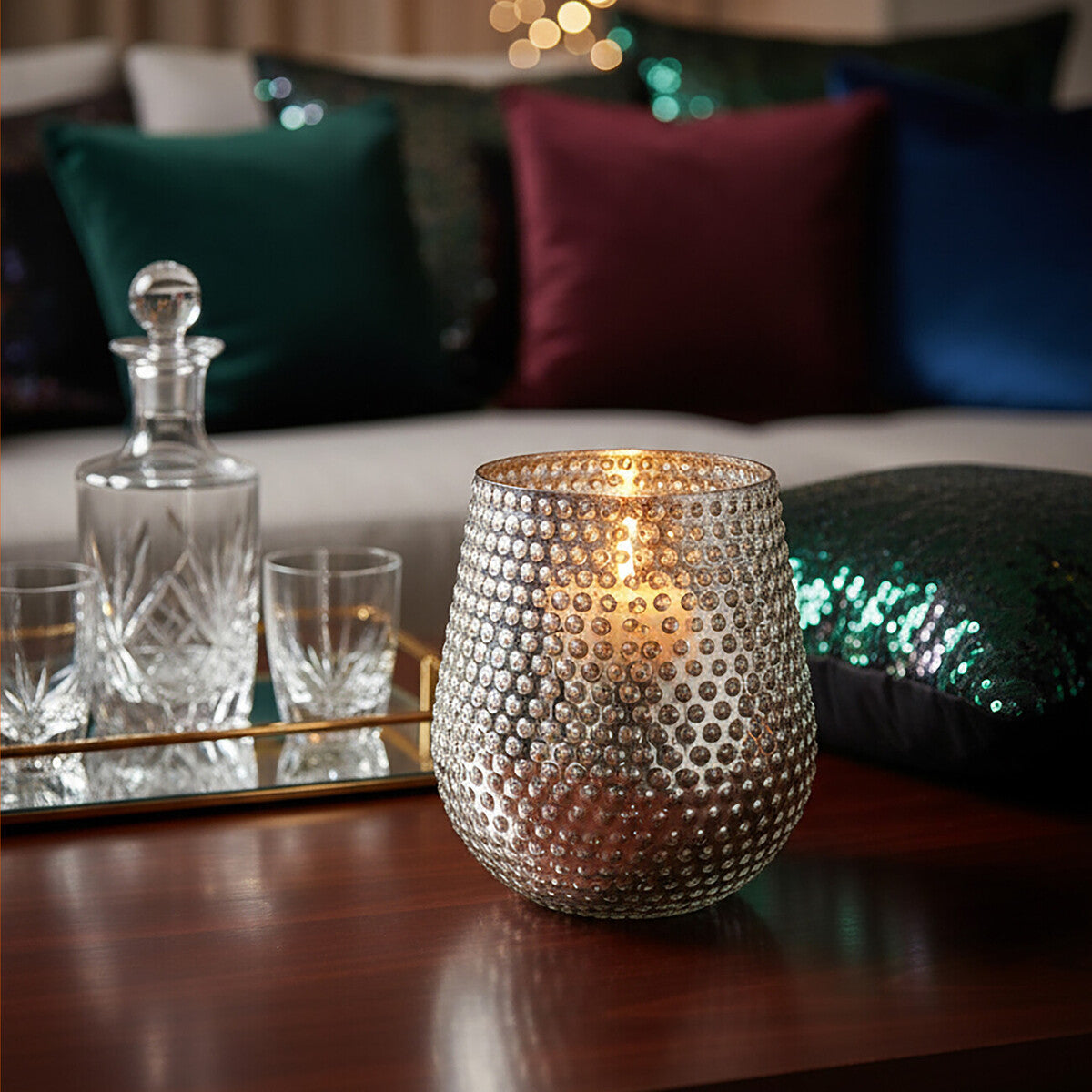 Decorative candle holder on a table with a blurred background of pillows and a mirror.