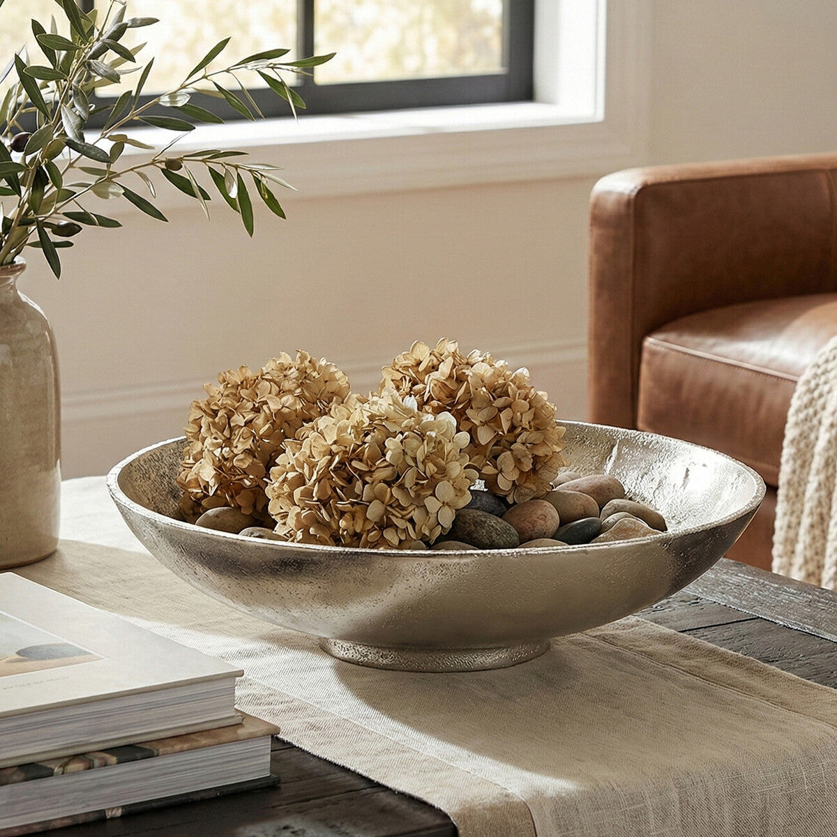 Decorative bowl with flowers and pebbles on a table in a living room setting.