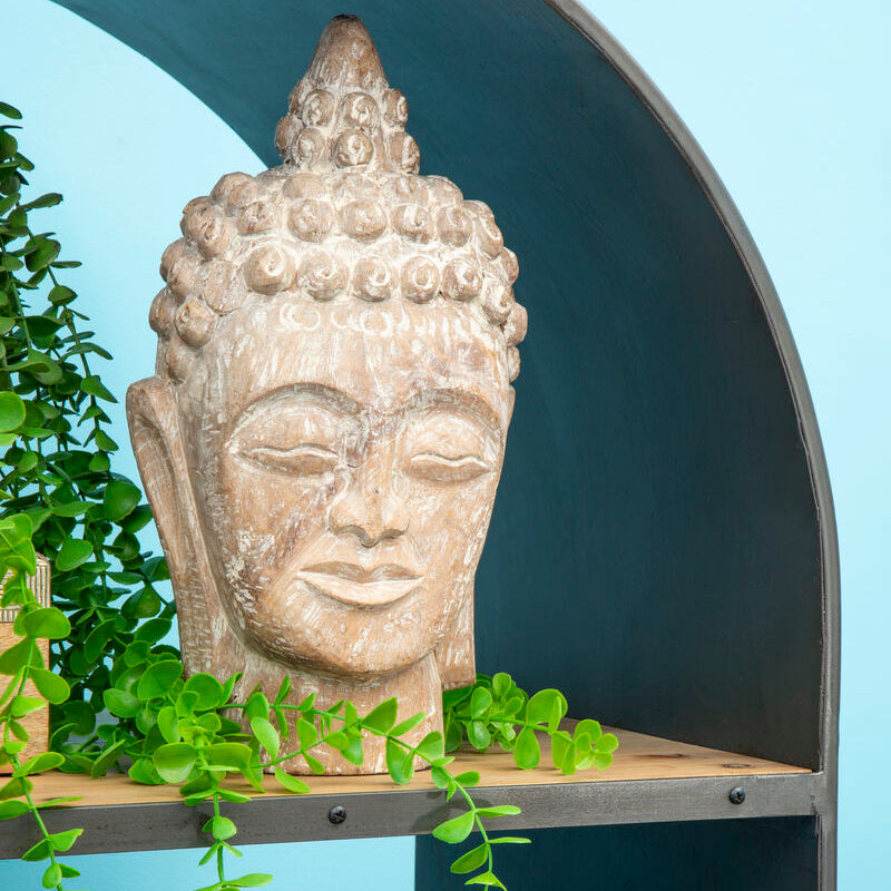 Stone Buddha head on a shelf with greenery against a blue wall