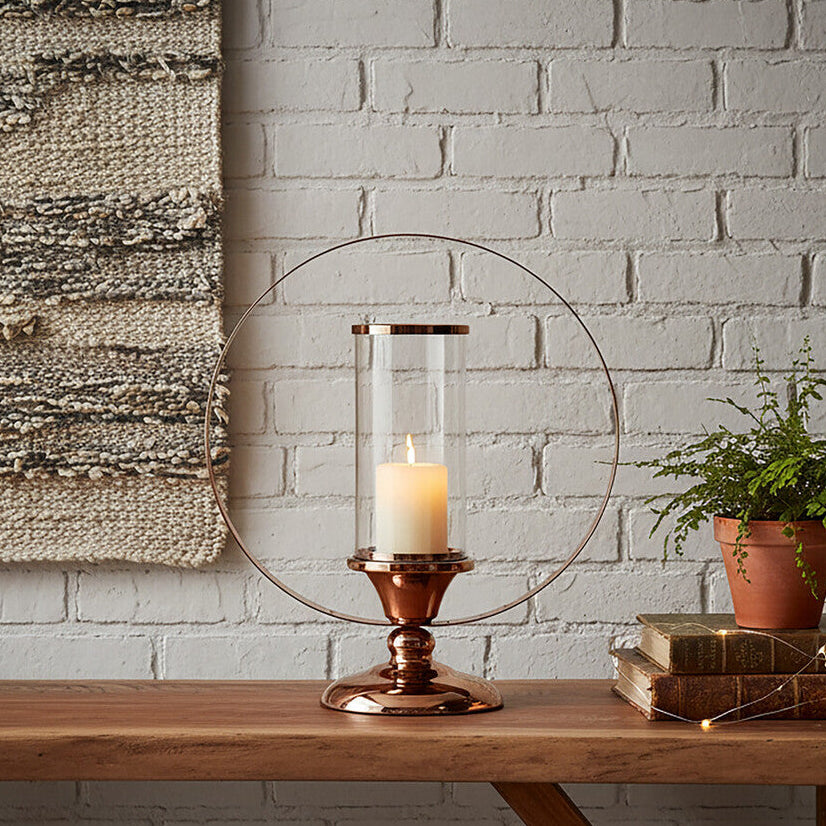 Wooden table with a candle holder, plant, and books against a white brick wall.