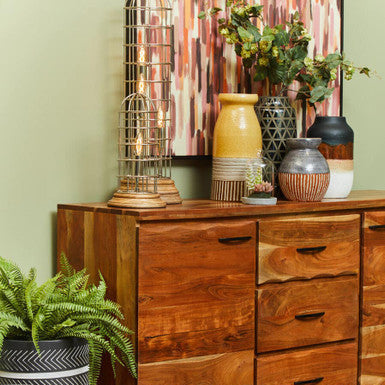Wooden dresser with decorative items and plants against a green wall