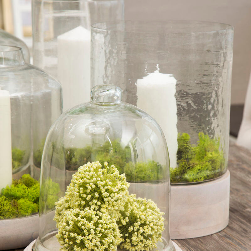 Decorative glass bell jar with greenery and candles on a wooden surface