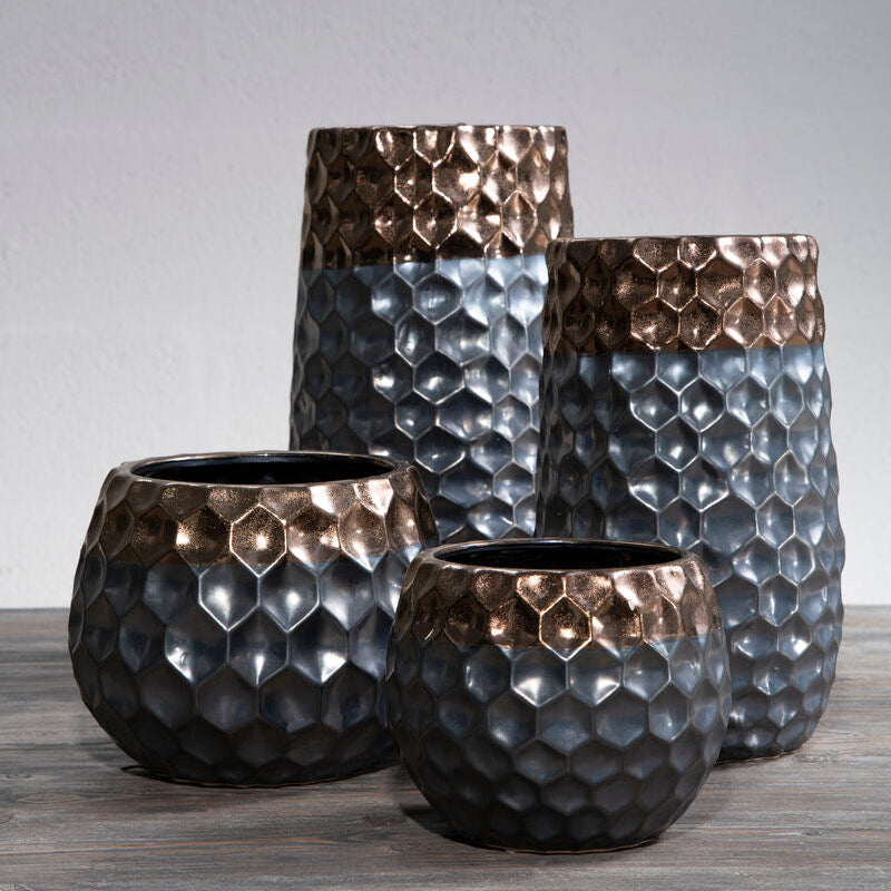 Set of four textured metal vases on a wooden surface with a gray background