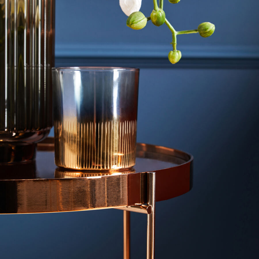 Gold candle holder on a small round table against a dark blue wall