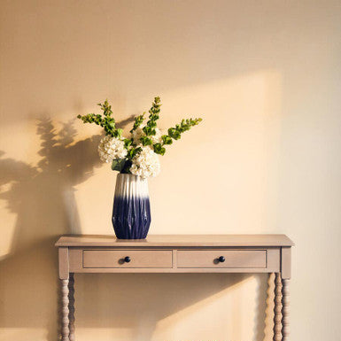 Wooden console table with a vase of flowers and a woven basket against a plain wall.