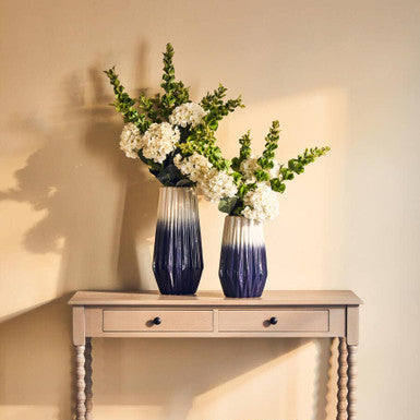 Two blue vases with flowers on a wooden console table against a beige wall.