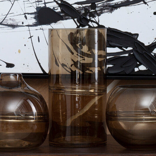 Three glass vases on a wooden surface with abstract black and white painting in the background