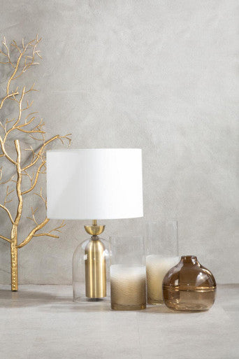 Decorative lamp with white shade and gold base, accompanied by candles and a vase on a neutral background.