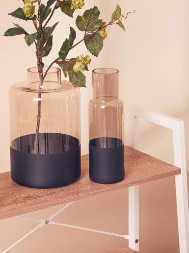 Two glass vases with black bases on a wooden surface.