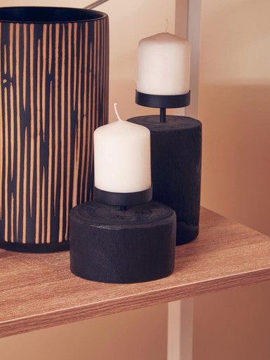 Three candles in black holders on a wooden surface with a neutral background