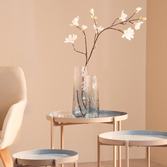 Set of small round tables with a vase of flowers on a beige wall background