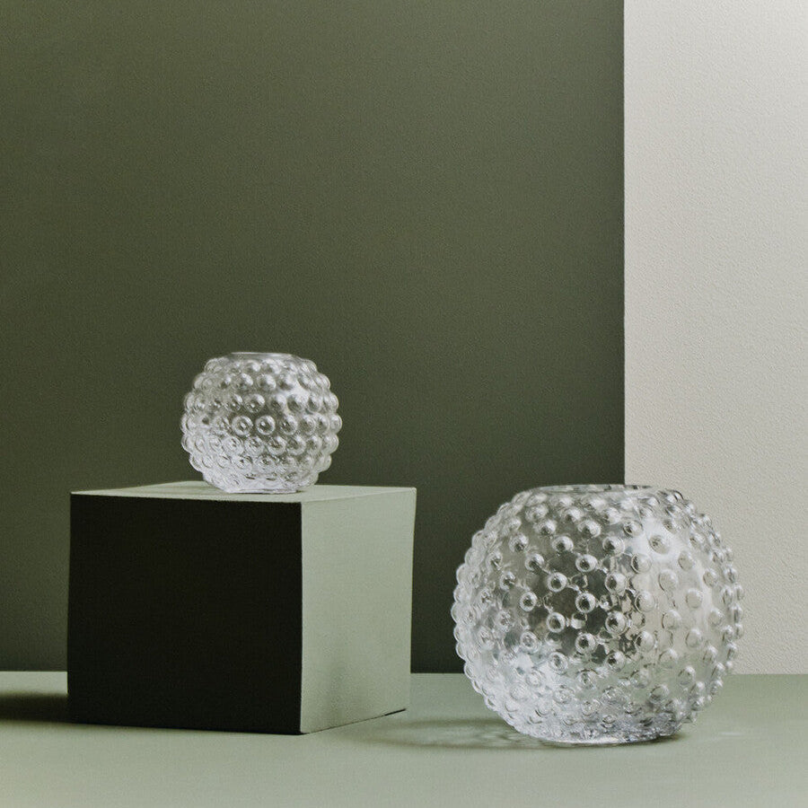 Two bubble-textured glass vases on a minimalistic setup with a green and white background.