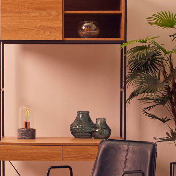 Wooden desk with shelves, black chair, and decorative items against a pink wall.
