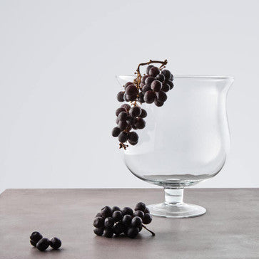 Clear glass goblet with grapes on a wooden surface and light gray background