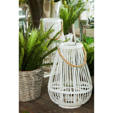 White woven lantern with a wooden handle next to a potted fern indoors.