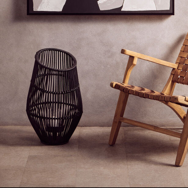 Abstract black and white artwork on a wall above a woven chair and black vase.