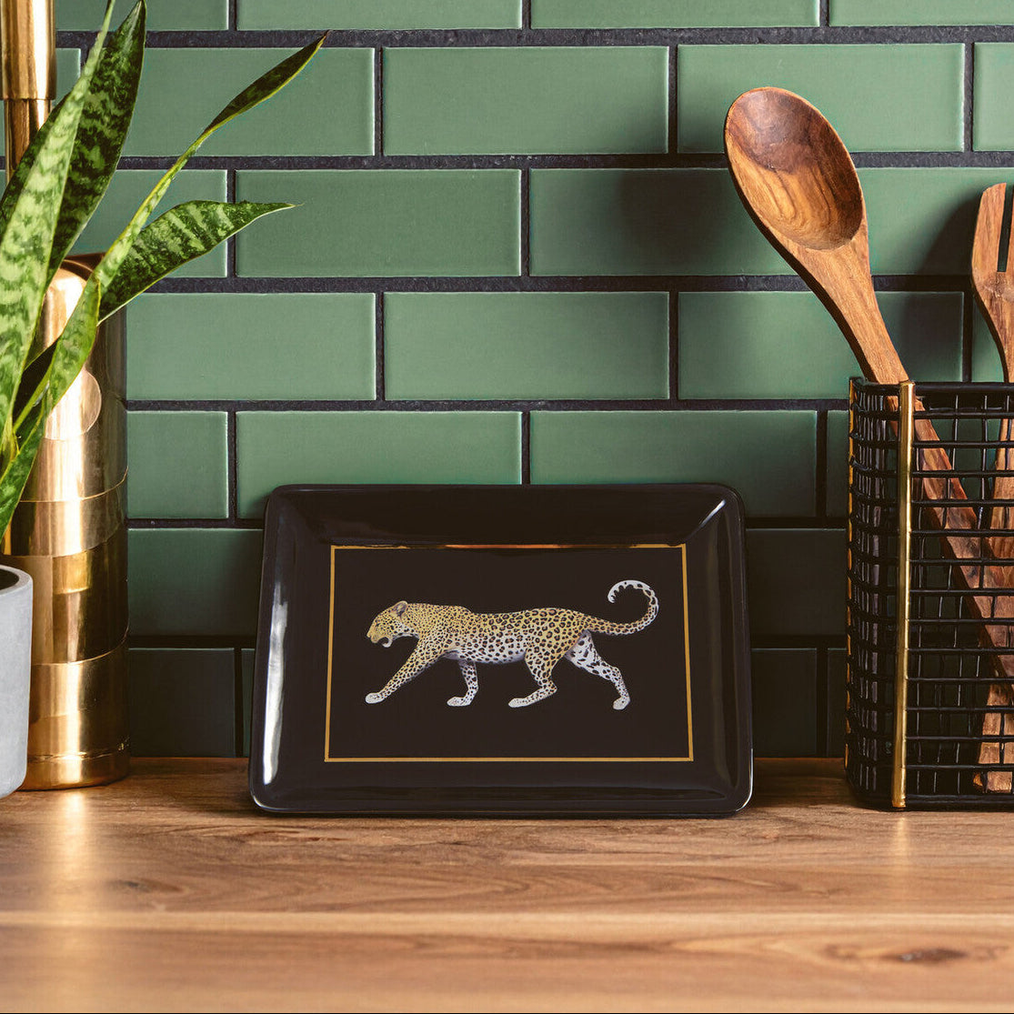 Decorative tray with a leopard design on a wooden surface against a green tiled wall.