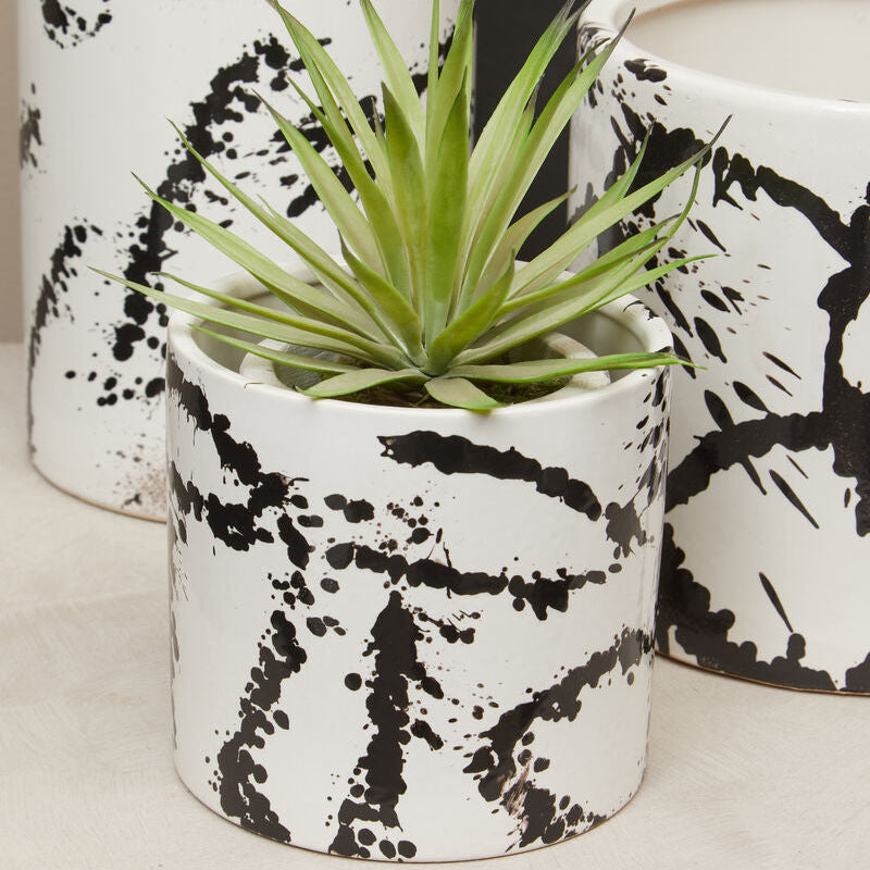 Ceramic pot with black abstract design containing a plant, placed on a light surface.