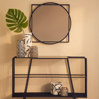 Black metal console table with round mirror and decorative items against a beige wall.