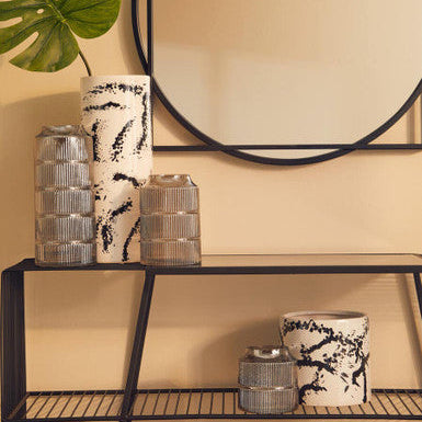 Decorative shelf with black and white vases and a mirror on a beige wall.