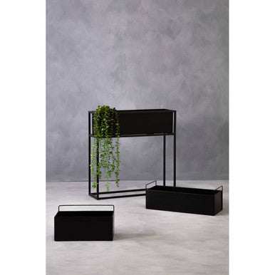 Black metal planters with green plants against a gray wall.