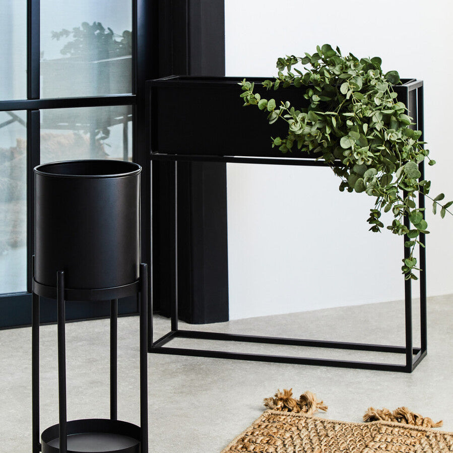 Black metal plant stand with a green plant on a light-colored floor.