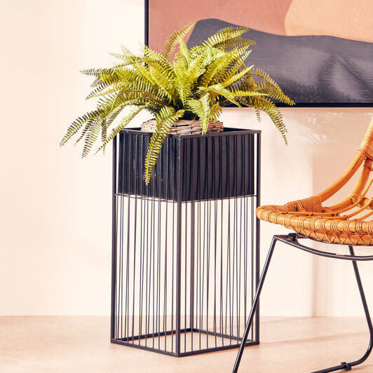 Wicker chair next to a plant in a decorative pot against a abstract wall art.