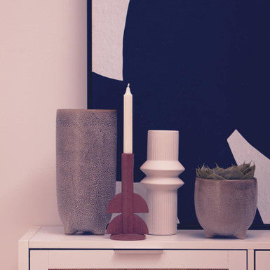Decorative items including a vase, candle, and plant on a white surface with a blue abstract painting in the background.