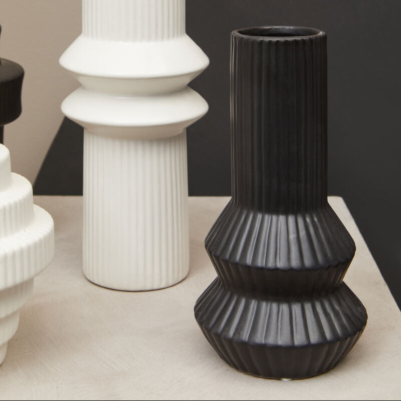 Three vases, two white and one black, on a surface with a neutral background.