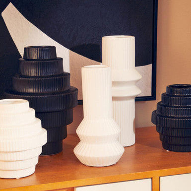 Set of black and white vases on a wooden surface with a abstract painting in the background.