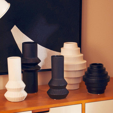 Set of black and white vases on a wooden surface with a abstract painting in the background.