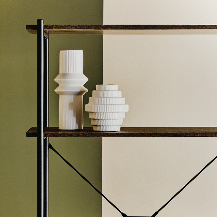 Two white textured vases on a wooden shelf against a green and beige wall.